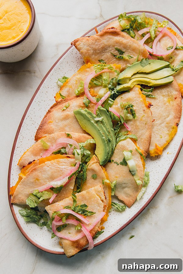 A platter of baked quesadillas topped with avocado and pickled onions.