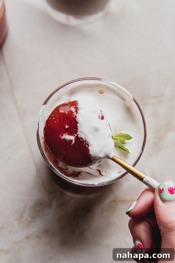 Sicilian Watermelon Delight 5 A spoon delicately scooping a bite of vibrant red Sicilian watermelon pudding from a clear glass cup, showing its smooth, firm texture, with a hint of green mint in the background.