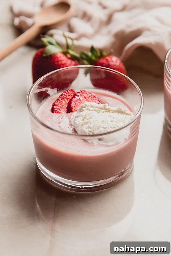 A beautifully set cup of creamy strawberries and cream pudding, ready to be enjoyed, with a spoon nearby and fresh berries in the background.