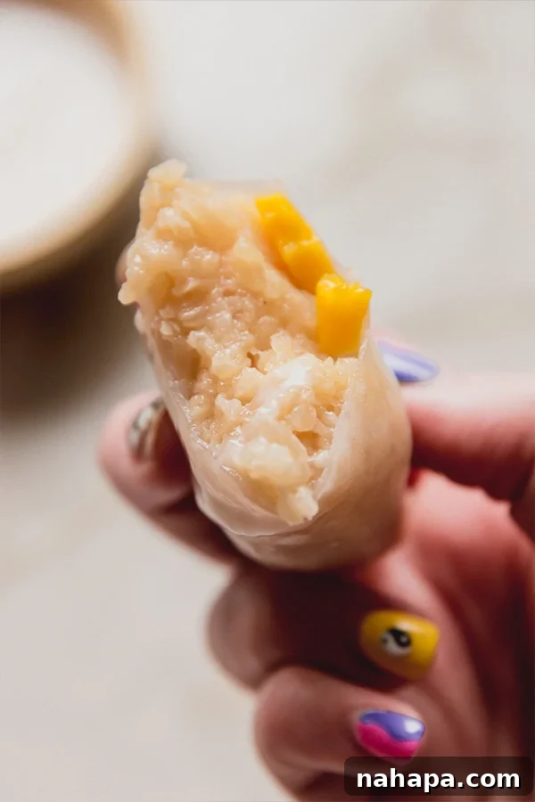 A mango sticky rice rolls being held in a hand with a bite taken out of it.