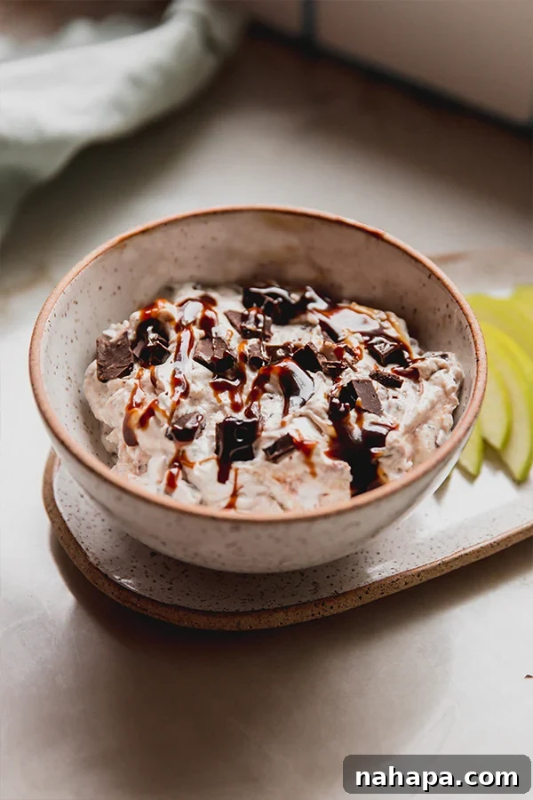 A beautifully presented bowl of dairy-free Snickers salad dip, surrounded by perfectly sliced green apple wedges, ready for serving on a rustic kitchen counter.
