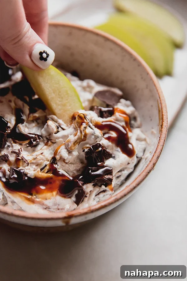 A bowl of snickers salad dip with an apple dipping into it.