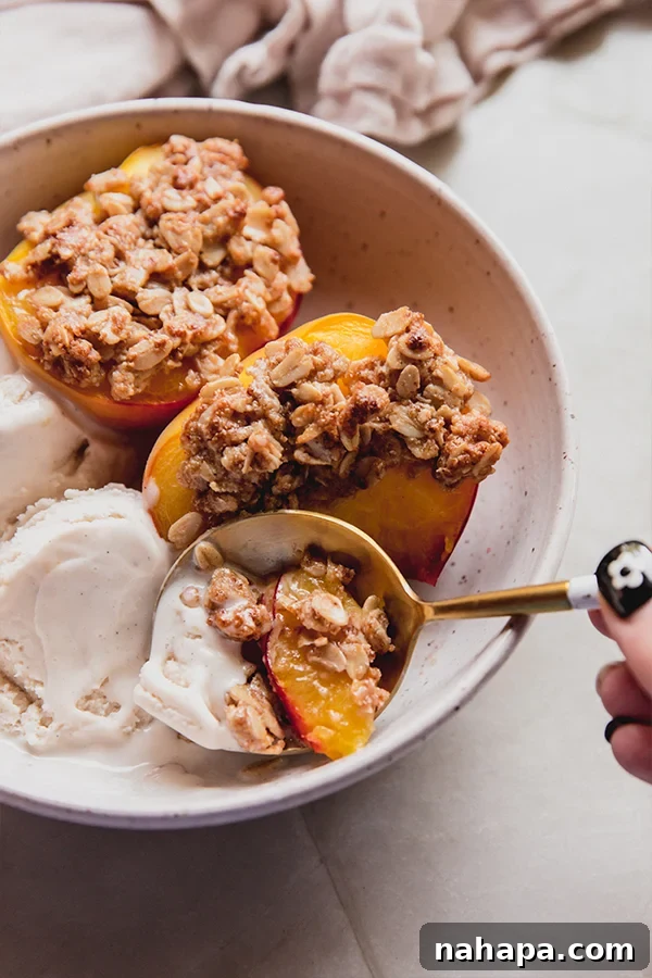 A bowl of air fryer peach crisp with dairy-free ice cream and a spoon taking a bite.