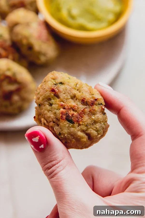 A close-up of a perfectly cooked zucchini chicken nugget, held delicately between fingers, showcasing its crispy exterior and inviting texture.