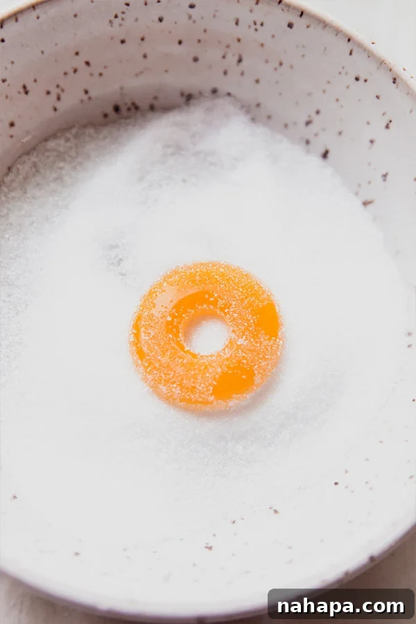 A single peach ring gummy being gently tossed in a bowl of granulated sweetener, preparing it for its classic finish.