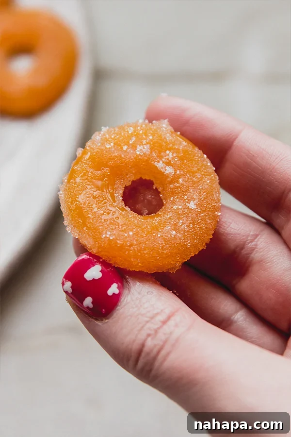 A hand holding a single, perfectly formed peach ring gummy, highlighting its appealing texture and natural color.