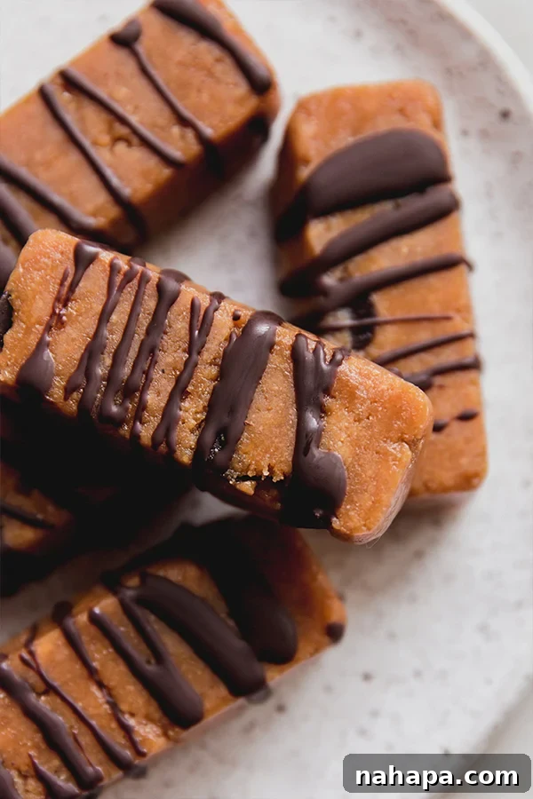 A stack of golden-brown cookie dough protein bars on a rustic white plate, garnished with a few scattered dairy-free chocolate chips.