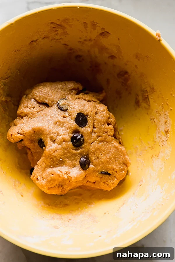 A large mixing bowl filled with the prepared cookie dough protein bar mixture, showing the thick, crumbly yet cohesive texture with visible chocolate chips.