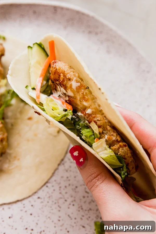 A crispy chicken snack wrap folded in a hand, ready to be eaten.