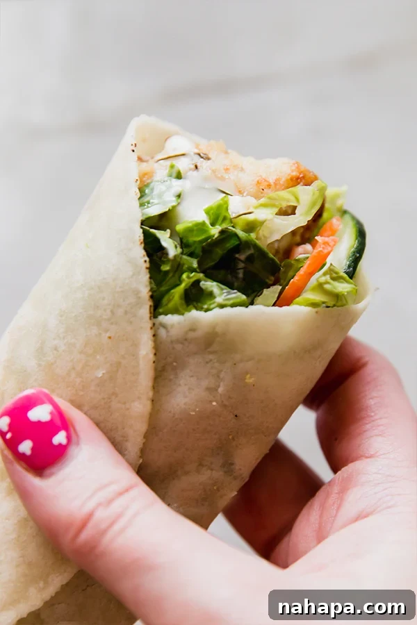 A crispy chicken snack wrap being held in a hand, showing its fillings.