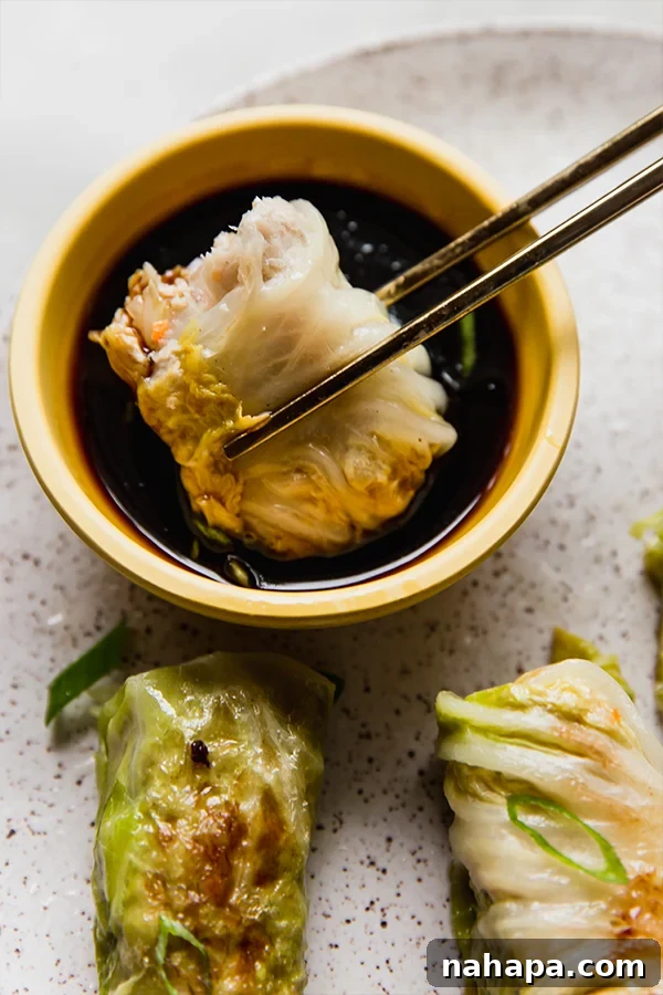 Chopsticks dipping a freshly steamed cabbage roll dumpling into a bowl of coconut aminos, highlighting a delicious and healthy meal.