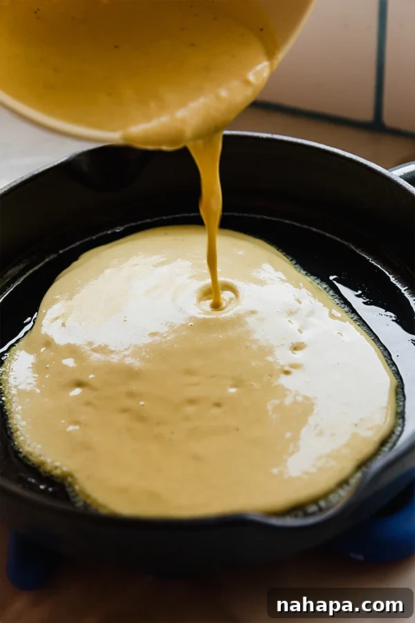 Socca: Effortless Golden Chickpea Flatbread 4 Chickpea flatbread batter being carefully poured from a mixing bowl into a sizzling hot cast iron skillet.