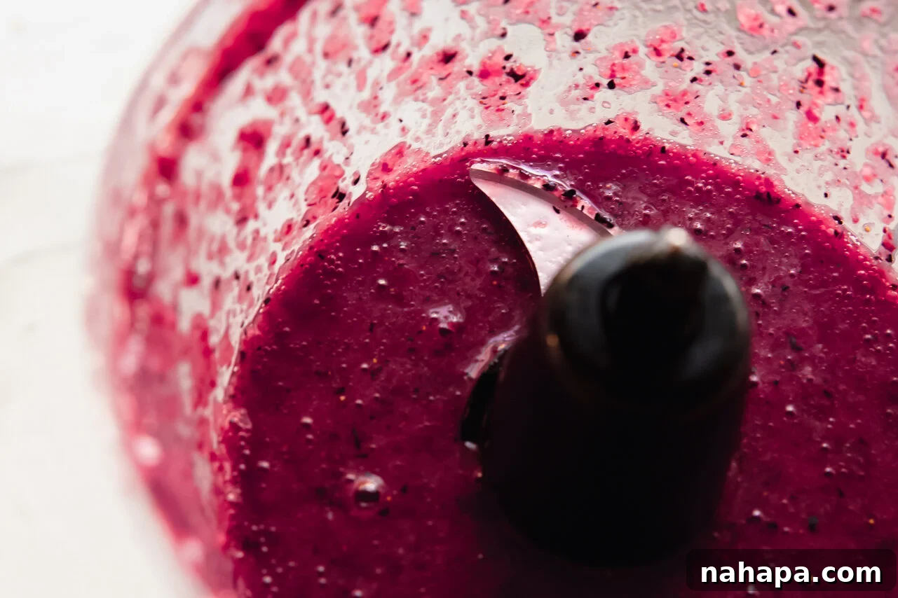 Fresh fruit (strawberries and blueberries) along with honey and lemon juice being blended in a food processor to create a smooth, vibrant fruit puree.