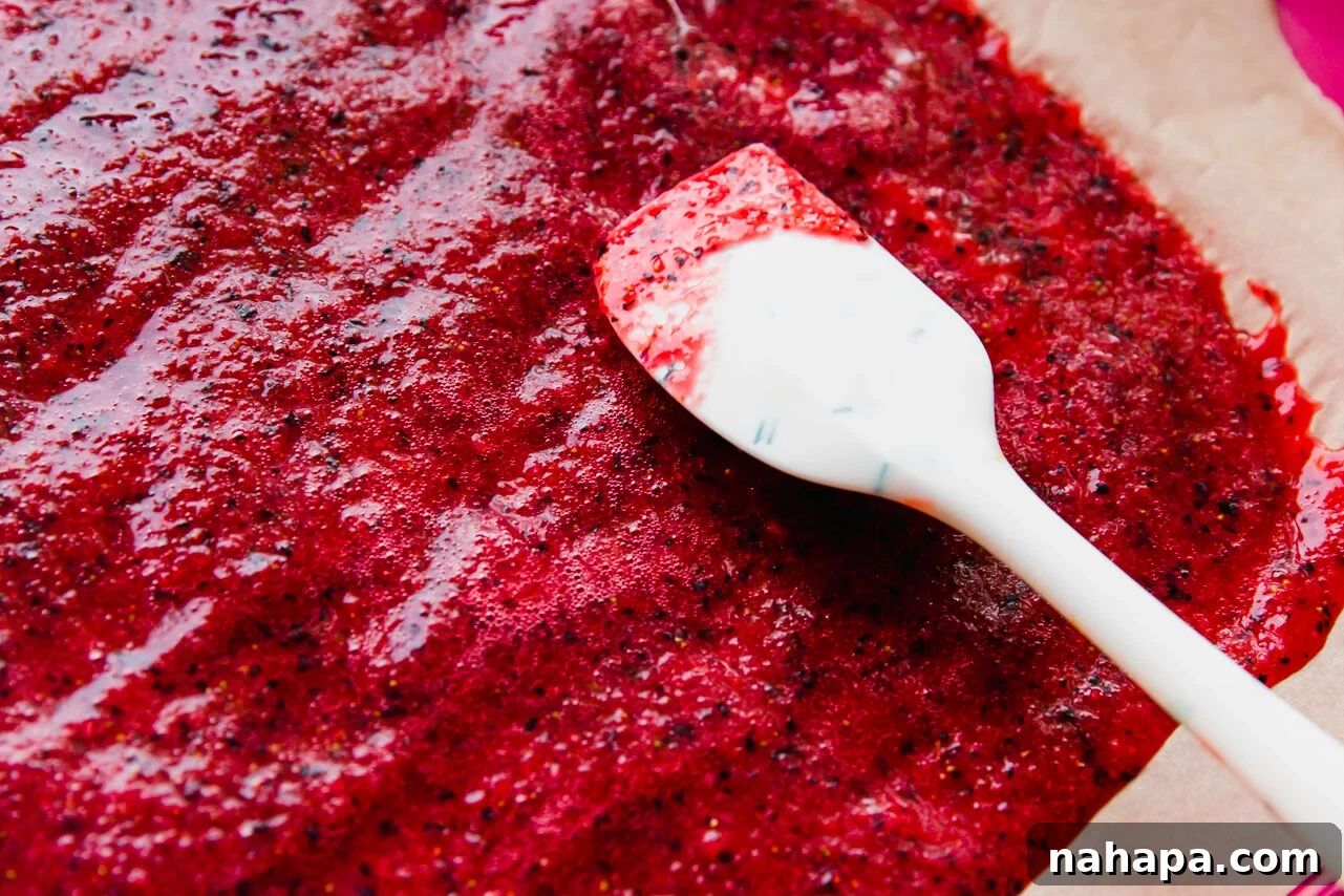 A smooth, vibrant fruit puree being carefully spread thinly and evenly onto a baking sheet lined with parchment paper using a flexible silicone spatula.