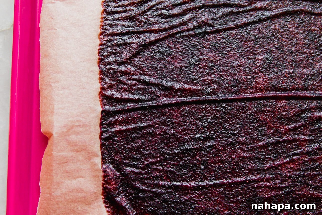 A large sheet of baked fruit leather, fully dried and pliable, resting on a parchment-lined baking sheet after dehydration in the oven, ready for cooling.