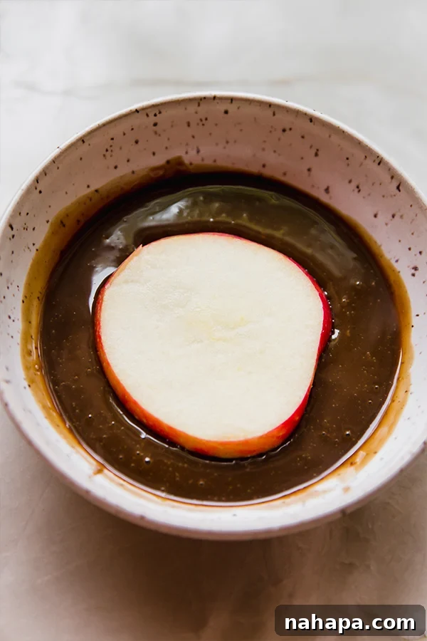 A crisp apple slice being carefully dipped into a bowl of luscious coconut milk caramel.