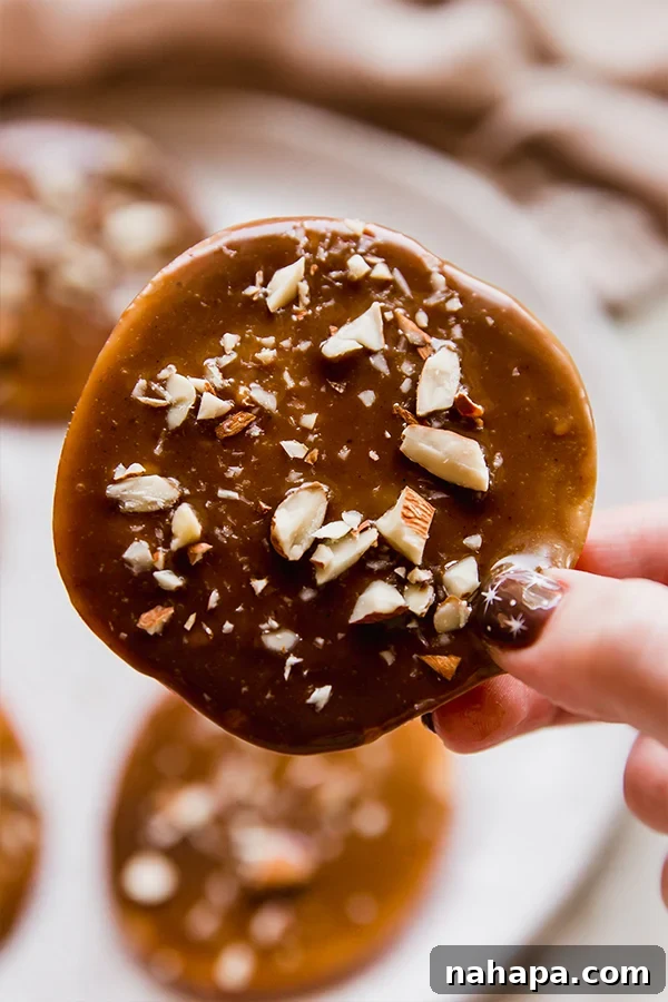 A hand holding a beautifully decorated caramel apple slice, topped with crushed almonds, ready to be enjoyed.