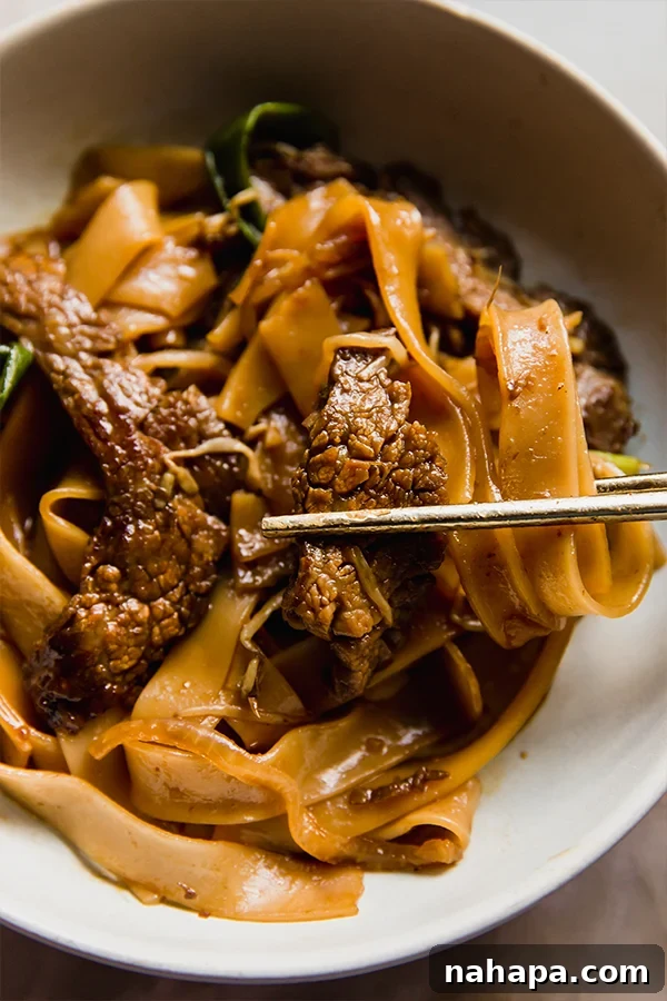 Wok-Kissed Gluten-Free Beef Chow Fun 6 A close-up shot of a bowl of gluten-free beef chow fun with chopsticks, capturing a bite of flavorful beef and noodles.