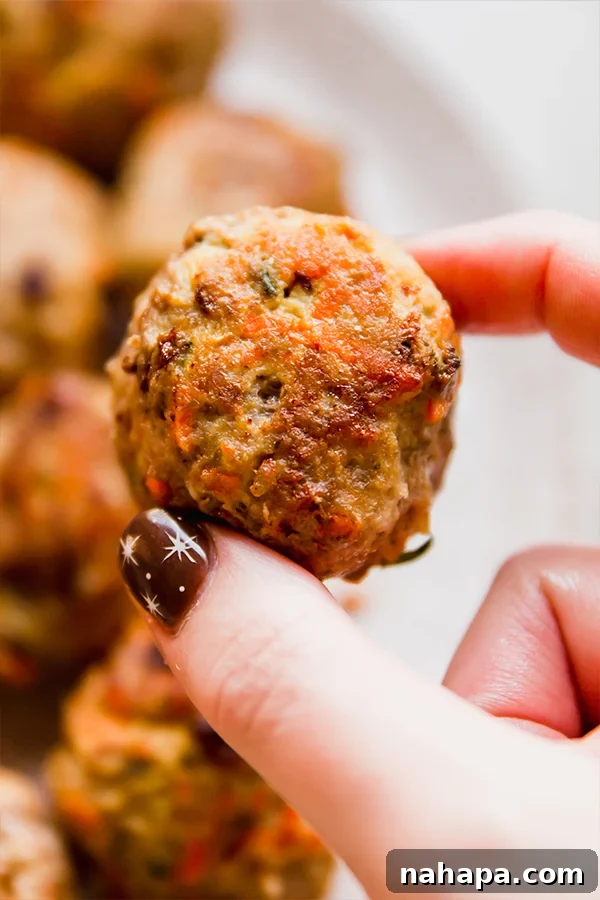 A hand holding a perfectly cooked hidden veggie meatball, showcasing its delicious texture.