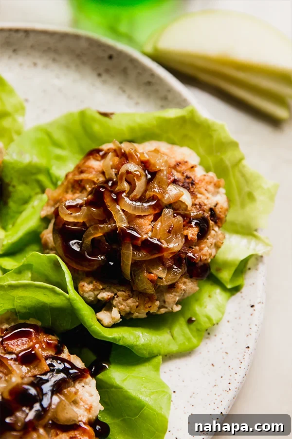 A beautifully plated dish featuring several Apple Chicken Burgers nestled in lettuce wraps, garnished with fresh herbs, ready to be enjoyed.