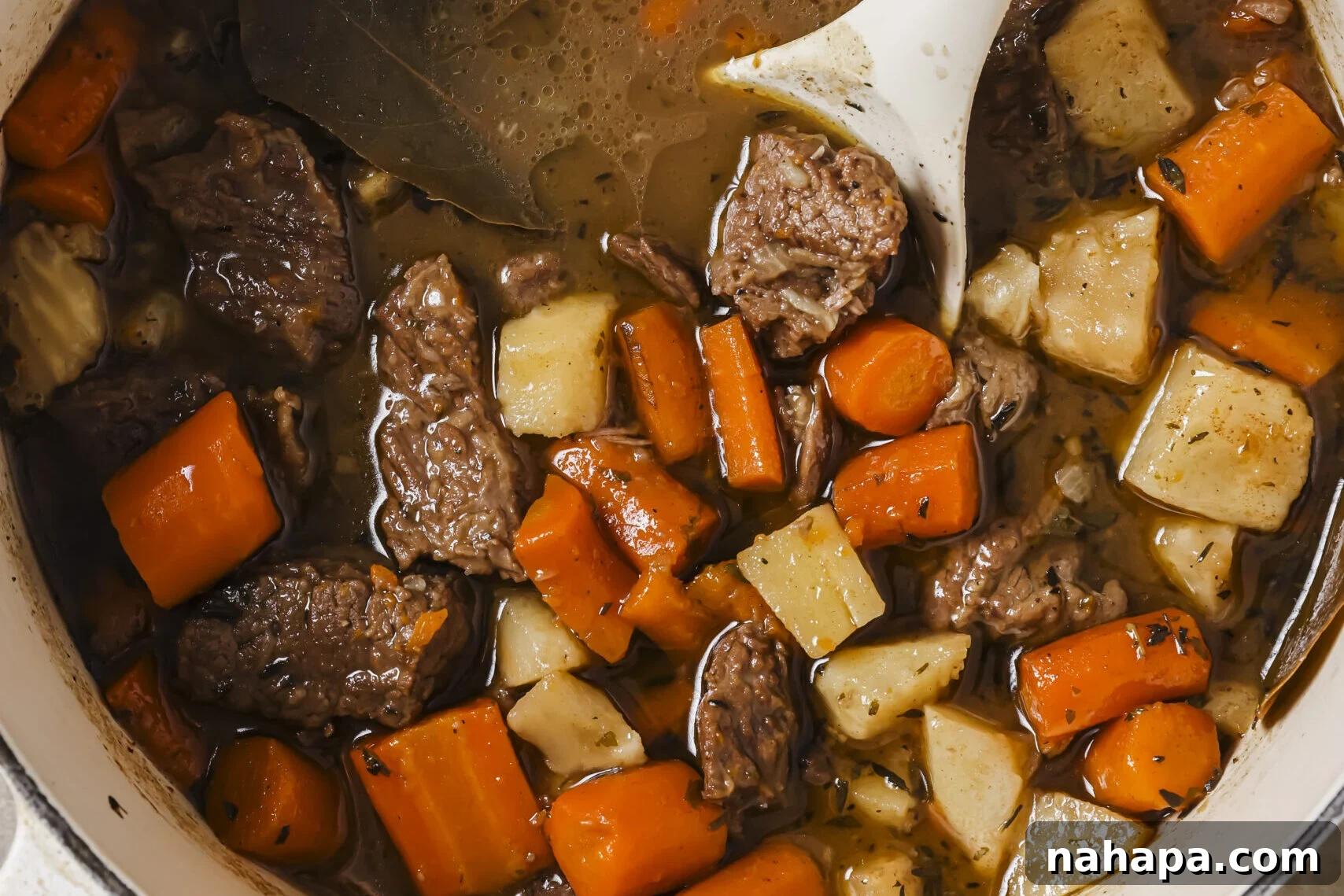 A Dutch oven filled with simmering beef stew, with a serving spoon resting inside.