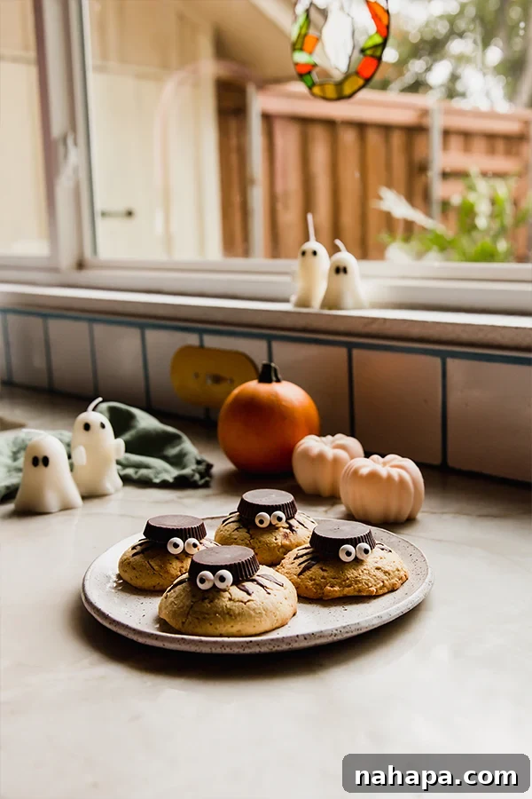 A plate of spooky Halloween spider cookies on a counter, surrounded by ghost candles and mini decorative squashes, creating a festive autumn scene.