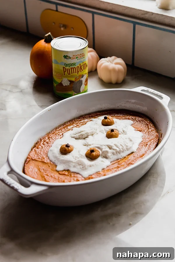 A finished baked pumpkin pudding, beautifully presented on a kitchen counter with decorative canned pumpkin and small mini pumpkins in the background.