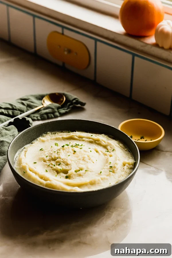 Creamy Instant Pot White Sweet Potato Mash 4 A bowl of creamy Instant Pot mashed white sweet potatoes, adorned with fresh chives, sits invitingly on a rustic wooden counter.