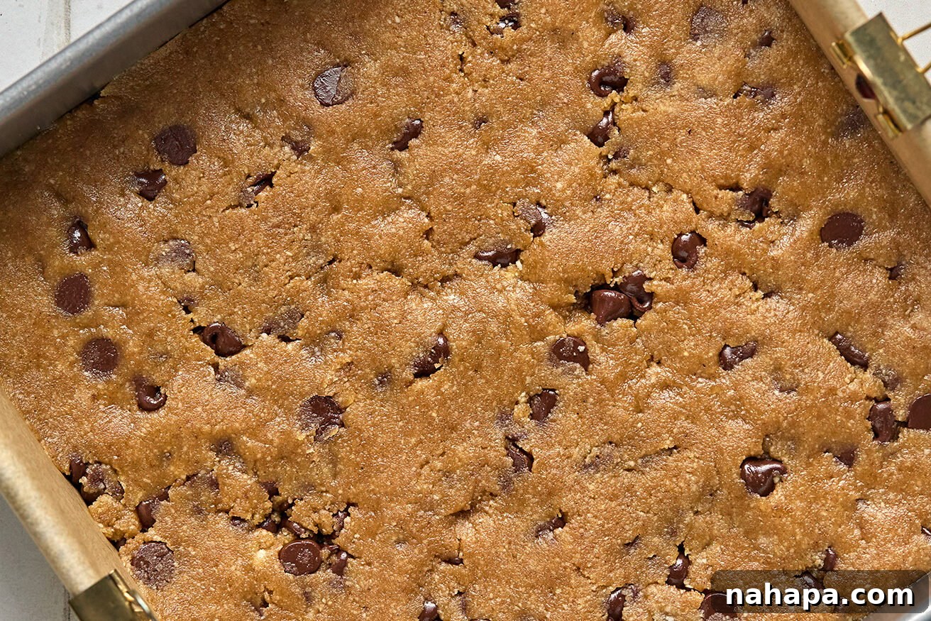 Spiced Gluten Free Pumpkin Chocolate Chip Cookie Bars 8 The prepared cookie bar dough, evenly pressed into the bottom of a square baking pan, forming the delicious base.