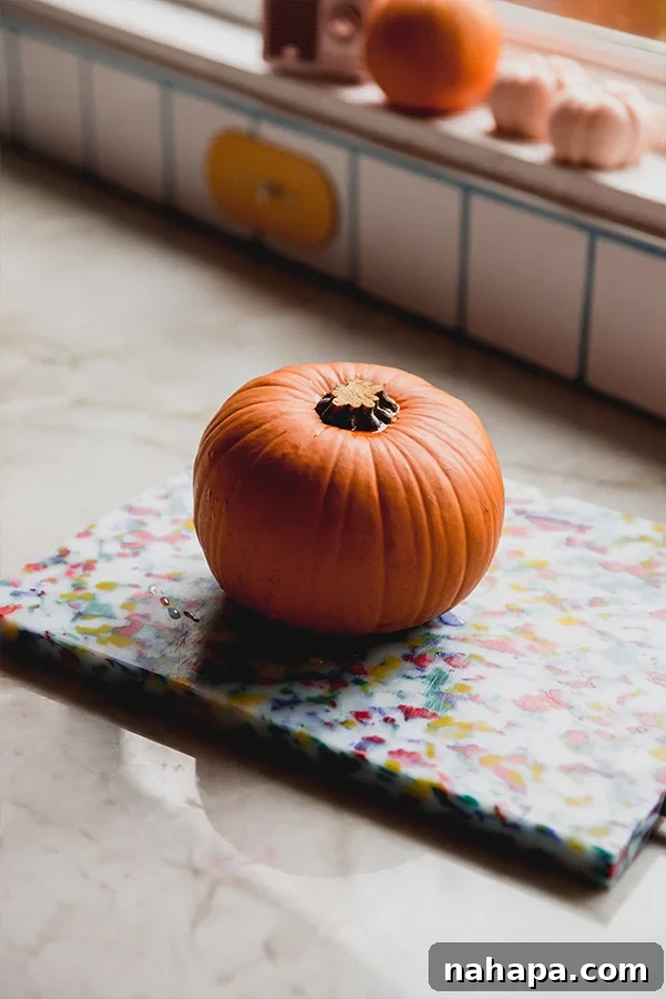 A fresh sugar pumpkin sits on a wooden counter, ready to be prepared and roasted for a homemade, dairy-free mac and cheese sauce.