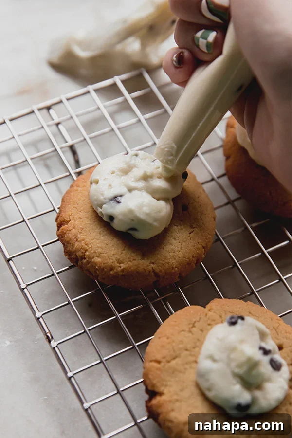 A close-up image of the thumbprint cookies being topped with the luscious cannoli cream using a piping bag.