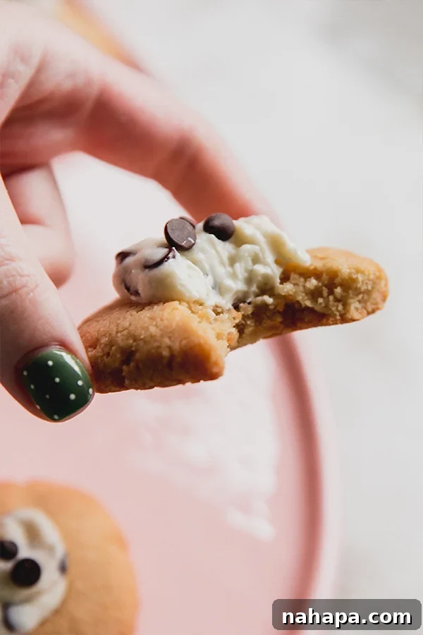 A cannoli thumbprint cookie being held in a hand, showing a bite taken out to reveal the creamy filling and tender cookie.
