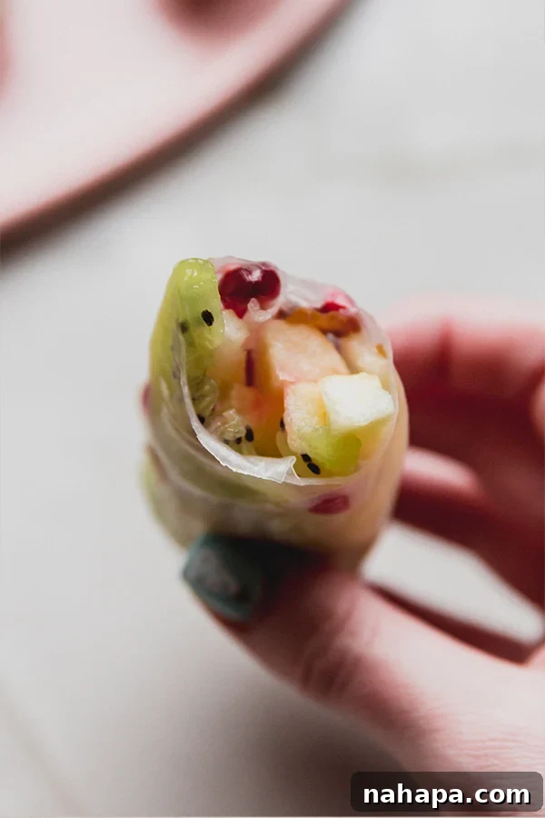 Winter Fruit Fresh Rolls 5 A close-up shot of a single winter fruit rice paper roll with a bite taken out, revealing the colorful layers of kiwi, apple, dates, and pomegranate inside.