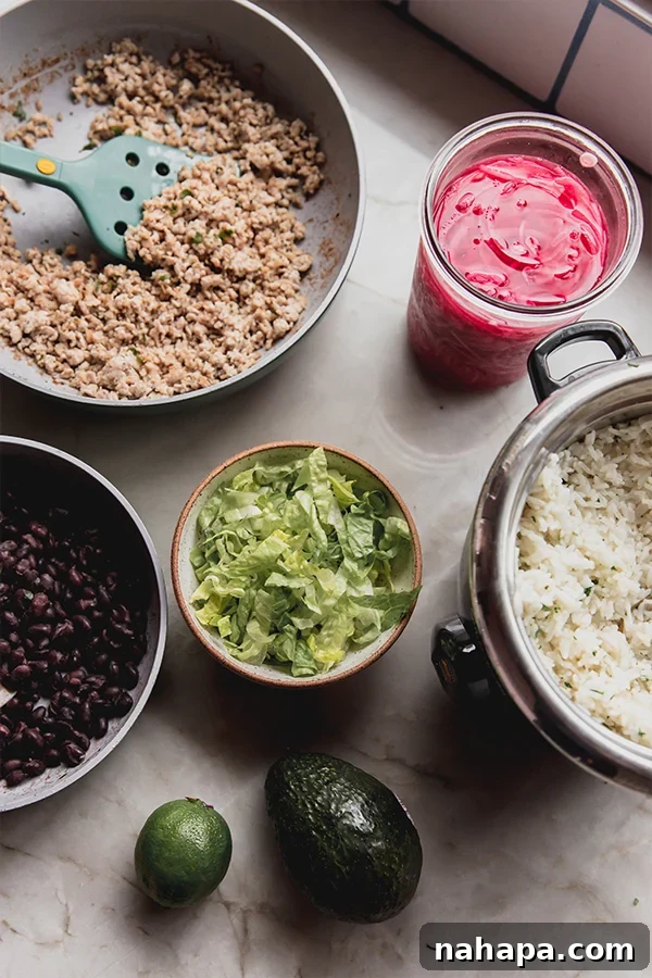 All the fresh ingredients laid out on a kitchen counter, including jasmine rice, ground chicken, various spices, lime, avocado, and lettuce, ready for preparing ground chicken chipotle bowls.