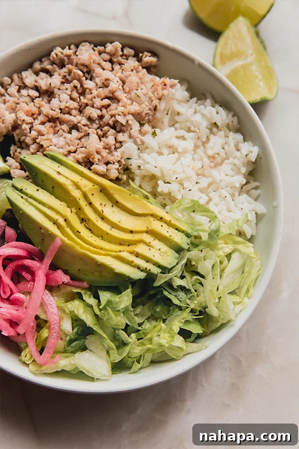 A close-up view of a perfectly assembled ground chicken chipotle style bowl, showcasing layers of rice, chicken, beans, avocado, and pickled red onions.