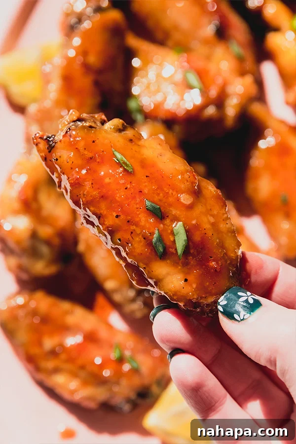 A lemon garlic chicken wing being held above a platter of wings, highlighting its crispy texture and glaze.