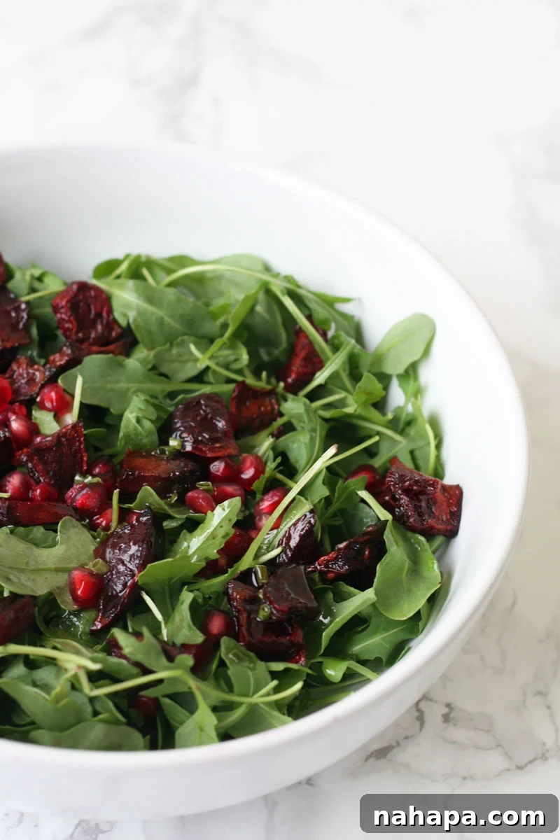Arugula salad in a white bowl with pomegranate seeds and roasted beets.