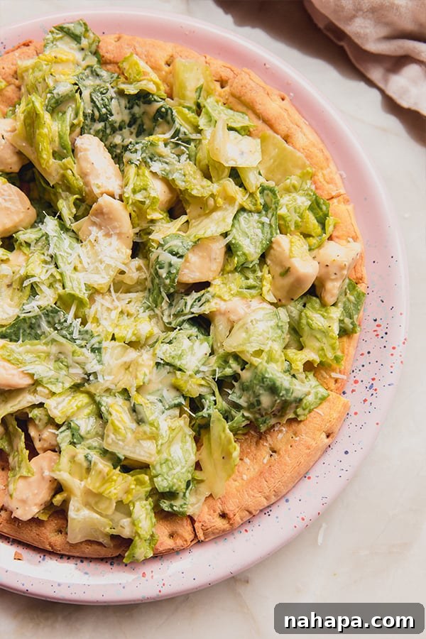 A vibrant chicken Caesar salad pizza on a rustic wooden board, garnished with fresh herbs and a slice ready to be enjoyed.