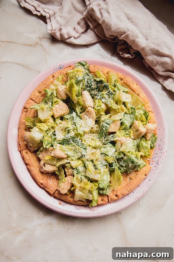 A close-up of a partially eaten chicken Caesar salad pizza slice on a plate, highlighting the fresh ingredients.