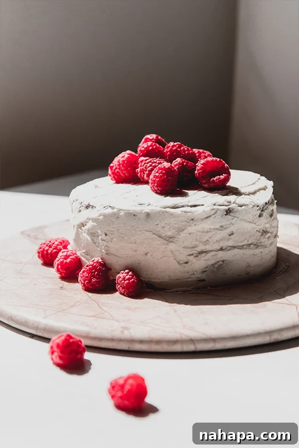 An entire gluten-free white chocolate raspberry cake, beautifully iced and adorned with fresh raspberries on top.