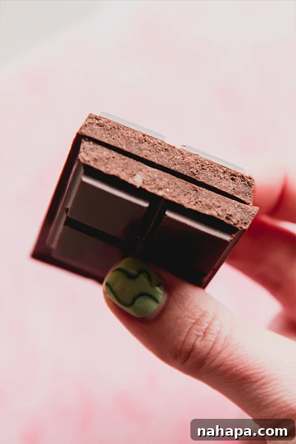 A homemade coconut milk chocolate bar broken in half and being held in a hand, revealing its creamy interior.