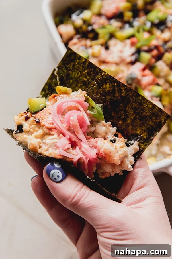 A piece of seaweed wrapped around the mini sushi bake topped with pickled onions.