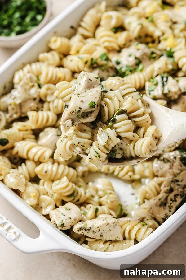 A serving spoon taking a spoonful of lemon chicken pasta bake out of the serving dish, showing creamy texture and chicken pieces.