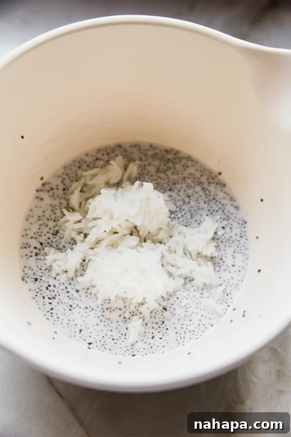 A close-up shot of a bowl where creamy chia pudding and cooked basmati rice are being gently mixed together with a spoon, showing the process of combining the base ingredients.