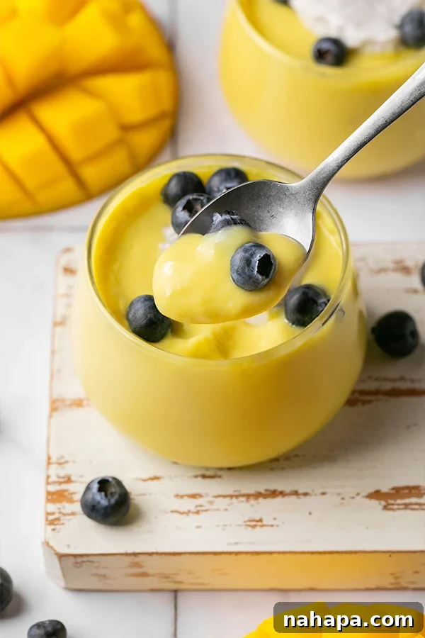 A close-up shot of a single serving of dairy-free mango pudding, with a spoon taking a scoop out of the creamy dessert.