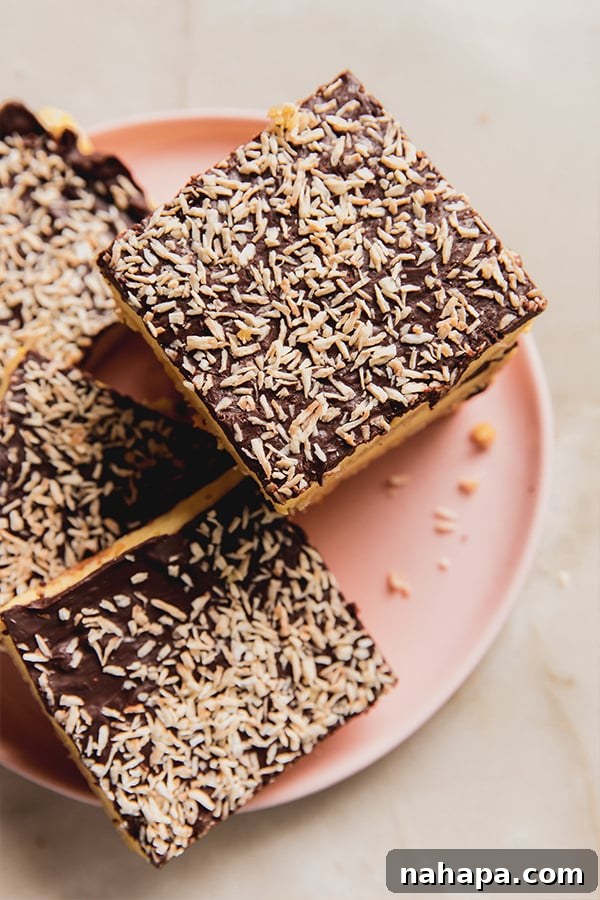 A plate featuring a close-up of multiple lemon coconut s'mores bars, each perfectly layered and ready to be savored. The golden crust, fluffy white marshmallow, and smooth chocolate ganache are visible, adorned with golden toasted coconut flakes.