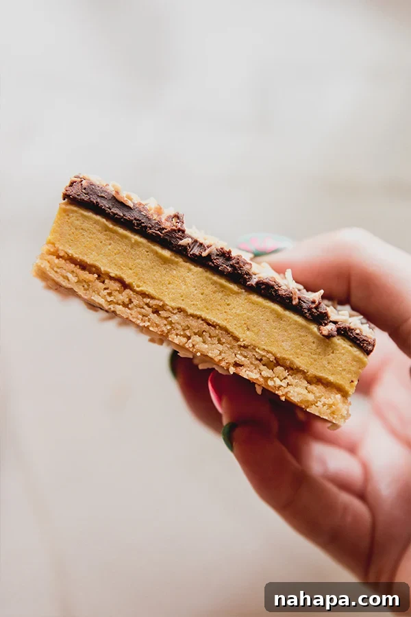 A hand holding a single lemon coconut s'mores bar, highlighting its delightful layers and making it look inviting and ready to eat. The textures of the crust, marshmallow, and toasted coconut are clearly visible.