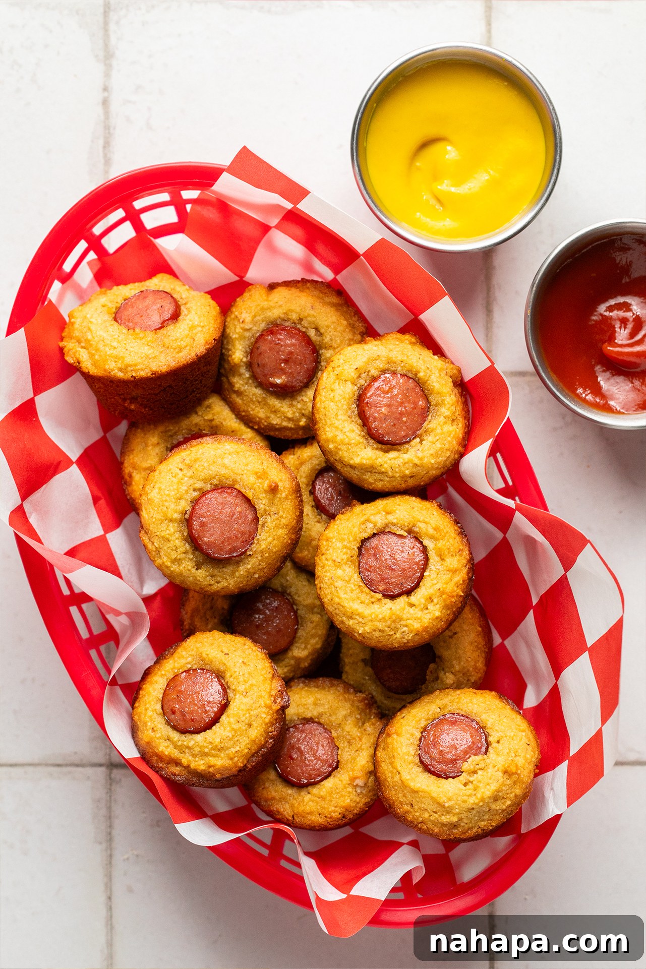 Basket of golden brown corn-free corn dog muffins, served with small dishes of mustard and ketchup, ready to be enjoyed.