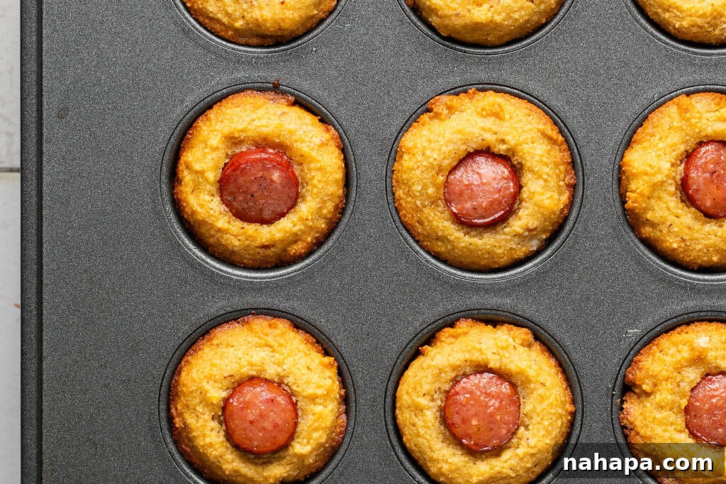 Baked corn-free corn dog muffins, golden brown and puffed, in a muffin tin.