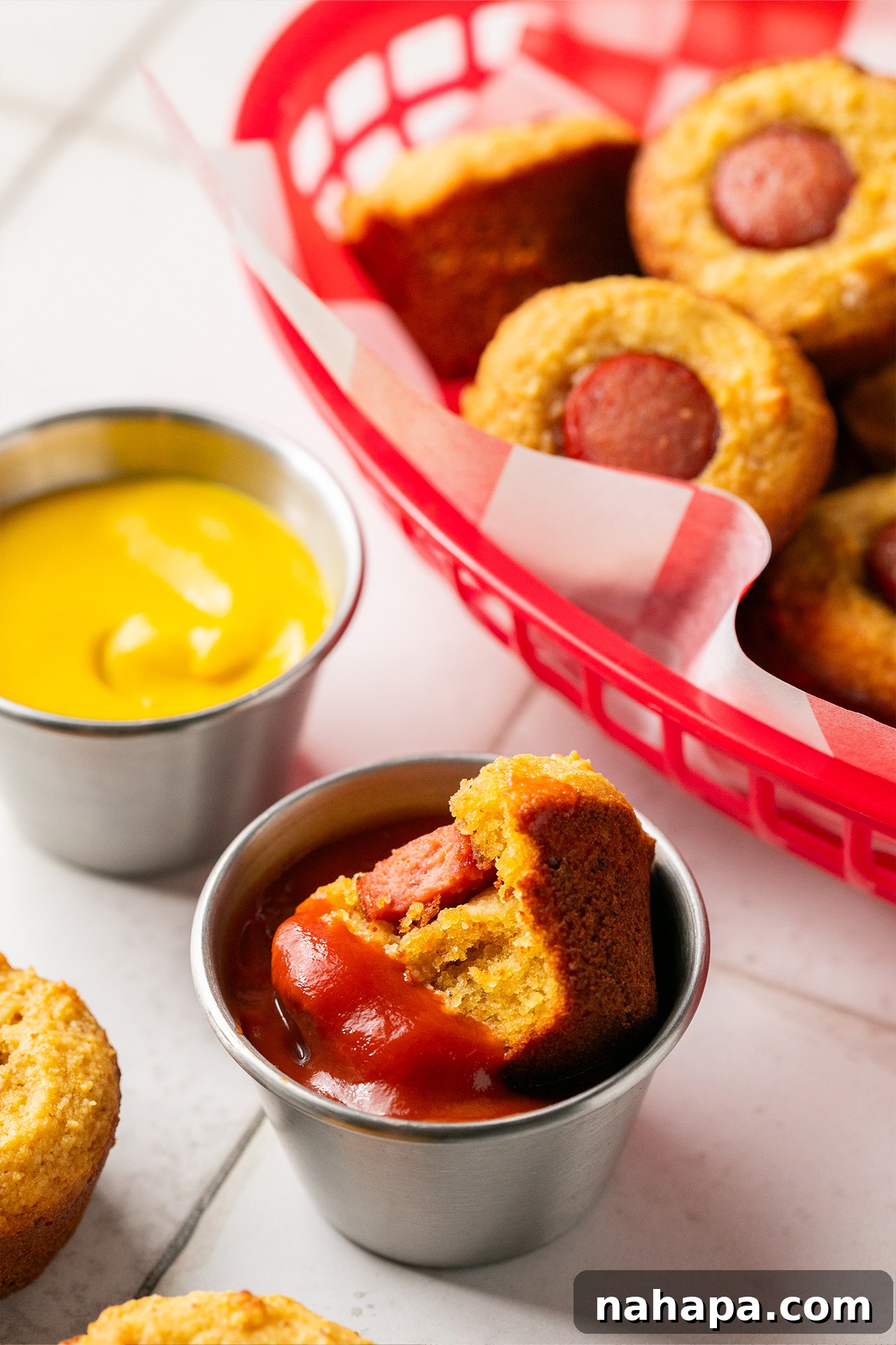 A corn-free corn dog muffin being dipped into a small dish of red ketchup, highlighting its golden exterior.